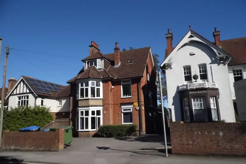 Two large Edwardian houses on East Street, Fareham, one red brick with white bay windows and tall chimneys, the other white-rendered with a balcony, behind low brick walls under a clear blue sky