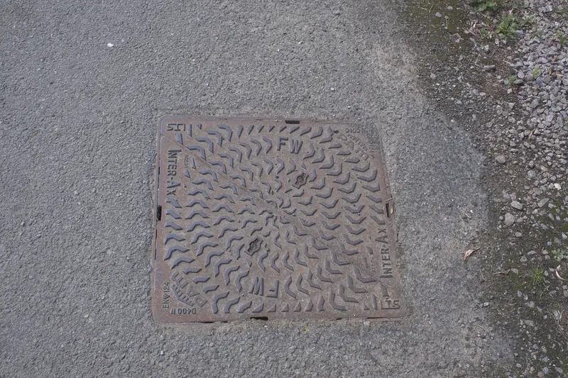Square cast-iron foul sewer cover stamped FW, set flush in a tarmac surface