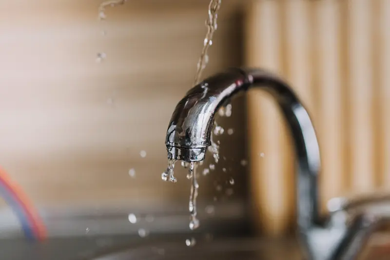 Water pouring and spraying in bright droplets from the curved chrome spout of a kitchen tap against a blurred wooden background